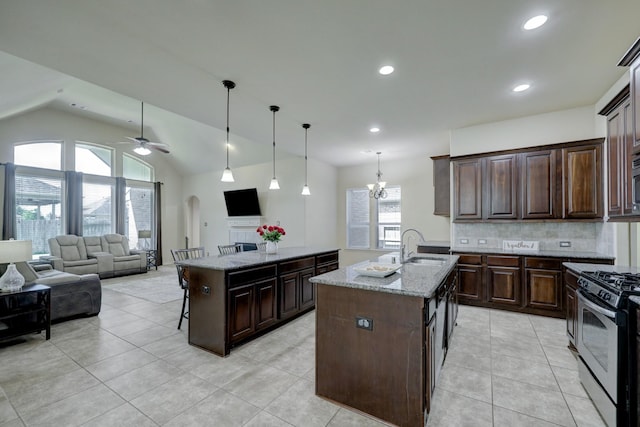 kitchen with pendant lighting, a kitchen island with sink, dark brown cabinets, light stone countertops, and gas range