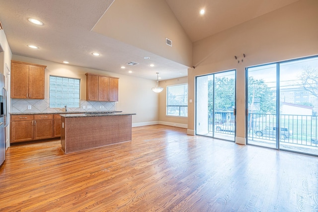 kitchen featuring stone counters, hanging light fixtures, a center island, decorative backsplash, and light wood-type flooring