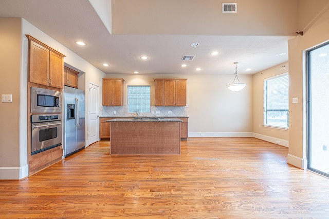 kitchen with decorative light fixtures, tasteful backsplash, a center island, stainless steel appliances, and light hardwood / wood-style flooring