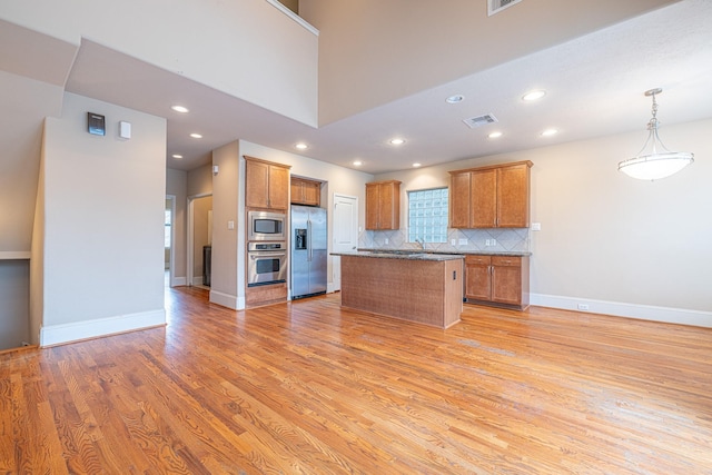 kitchen with pendant lighting, light hardwood / wood-style flooring, appliances with stainless steel finishes, a center island, and decorative backsplash