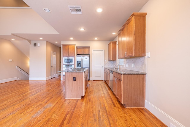 kitchen featuring sink, stainless steel appliances, light hardwood / wood-style floors, a kitchen island, and dark stone counters