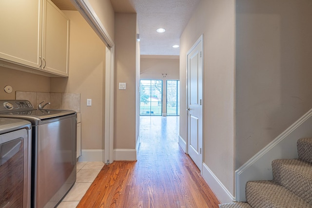 laundry room with cabinets, washer and dryer, a textured ceiling, and light wood-type flooring