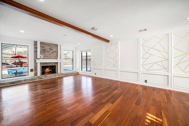 unfurnished living room featuring beamed ceiling, a fireplace, hardwood / wood-style floors, and a textured ceiling