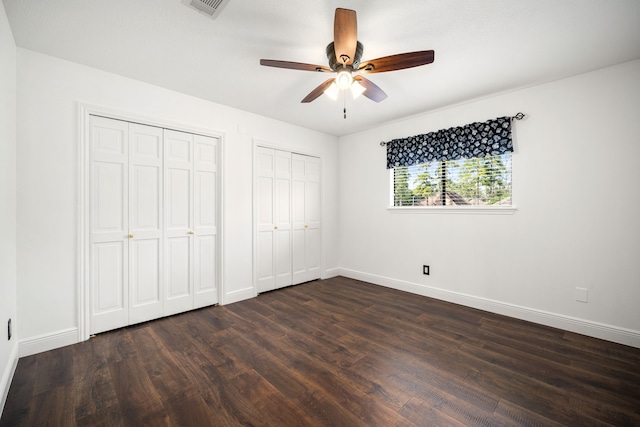 unfurnished bedroom with multiple closets, ceiling fan, and dark wood-type flooring