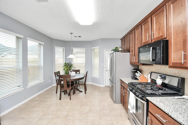 kitchen with hanging light fixtures, stainless steel gas range oven, light stone countertops, light tile patterned flooring, and decorative backsplash