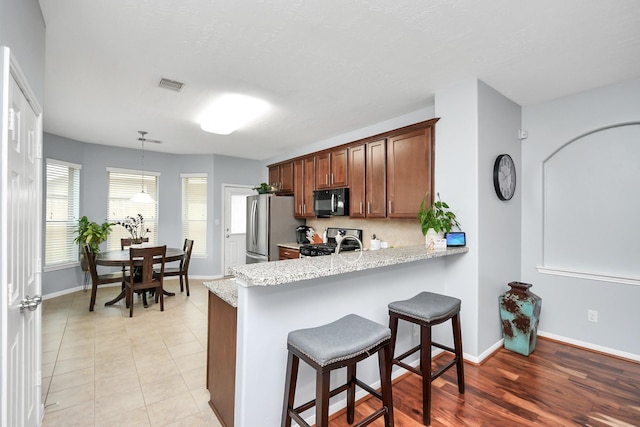 kitchen featuring stove, hanging light fixtures, stainless steel fridge, and light stone countertops