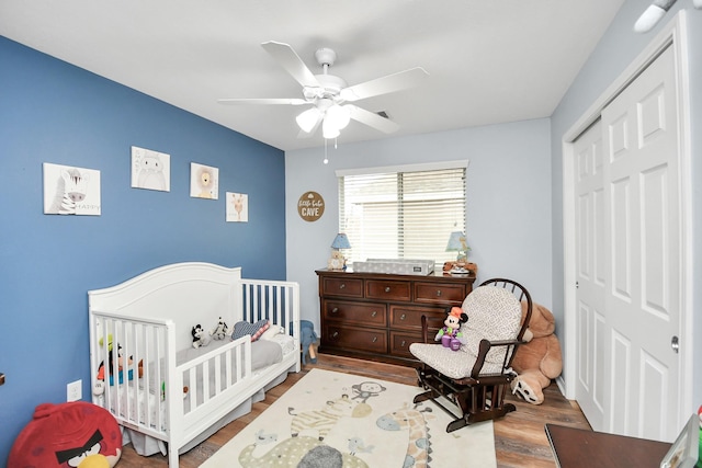 bedroom featuring a crib, hardwood / wood-style floors, ceiling fan, and a closet