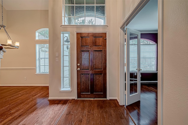 foyer entrance with dark wood finished floors, baseboards, french doors, a towering ceiling, and a chandelier