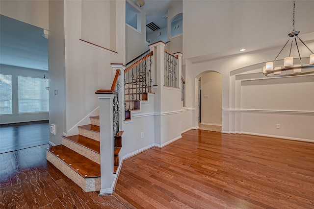 stairway featuring a chandelier, wood finished floors, arched walkways, baseboards, and a towering ceiling