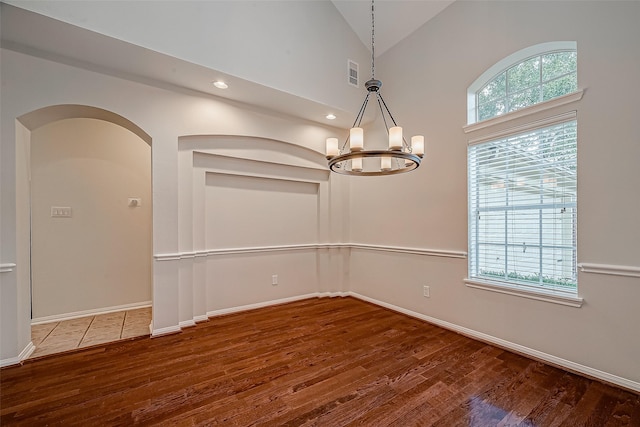 unfurnished dining area with dark wood-type flooring, high vaulted ceiling, and an inviting chandelier