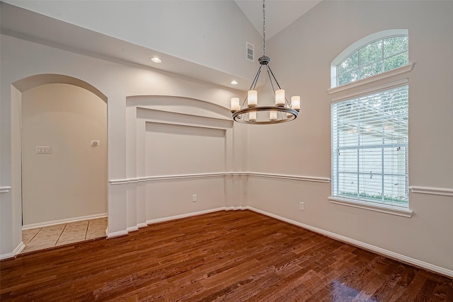 empty room with a chandelier, wood finished floors, lofted ceiling, baseboards, and recessed lighting