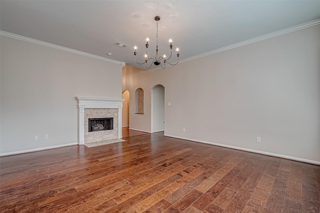 unfurnished living room featuring wood finished floors, a chandelier, crown molding, arched walkways, and baseboards