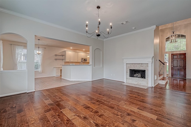 unfurnished living room with a chandelier, wood finished floors, crown molding, a fireplace, and arched walkways