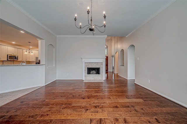 unfurnished living room featuring ornamental molding, wood finished floors, a chandelier, a fireplace with flush hearth, and a sink