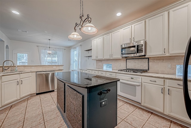 kitchen featuring sink, appliances with stainless steel finishes, hanging light fixtures, a center island, and light stone countertops