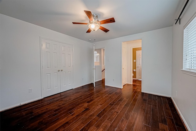 unfurnished bedroom with dark wood-style floors, baseboards, a closet, and ceiling fan
