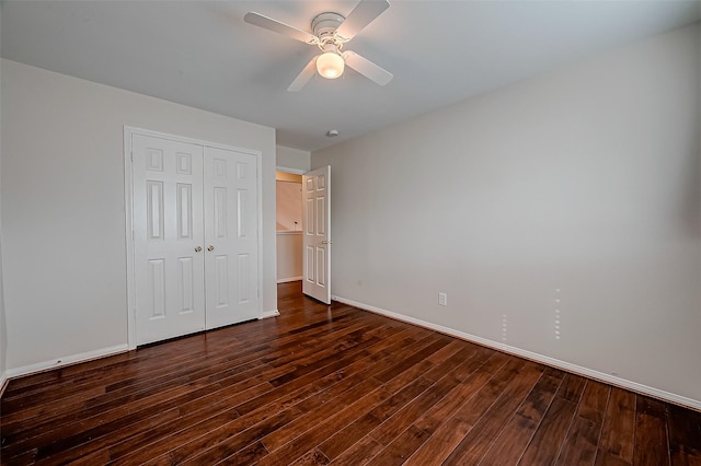 unfurnished bedroom featuring baseboards, dark wood-type flooring, a closet, and a ceiling fan