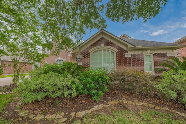 view of front of property featuring brick siding and roof with shingles