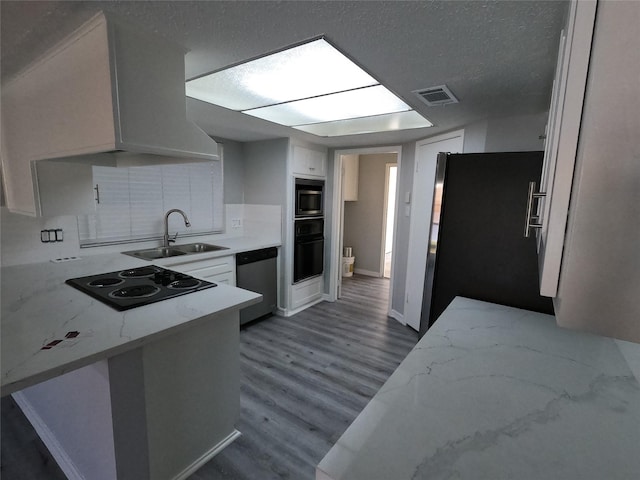 kitchen with dark wood-type flooring, sink, kitchen peninsula, white cabinets, and black appliances