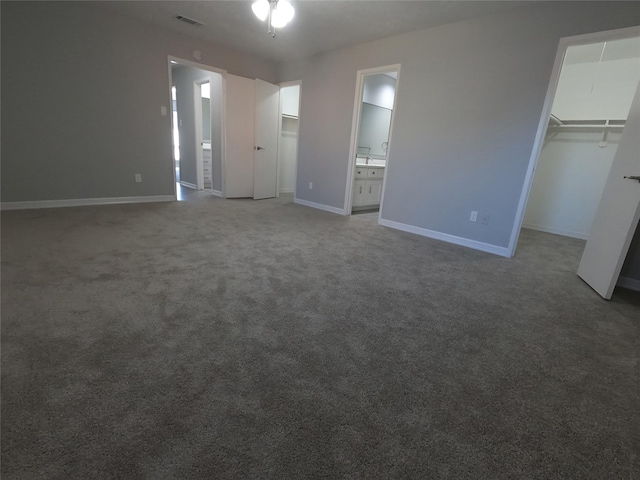 unfurnished bedroom with a spacious closet, ensuite bath, a closet, and carpet