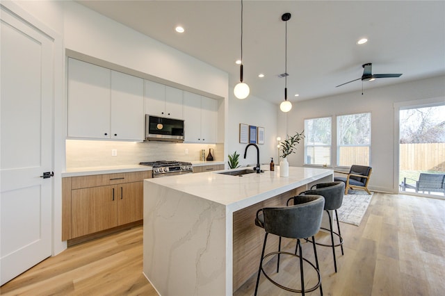 kitchen featuring a sink, white cabinets, appliances with stainless steel finishes, a center island with sink, and decorative light fixtures