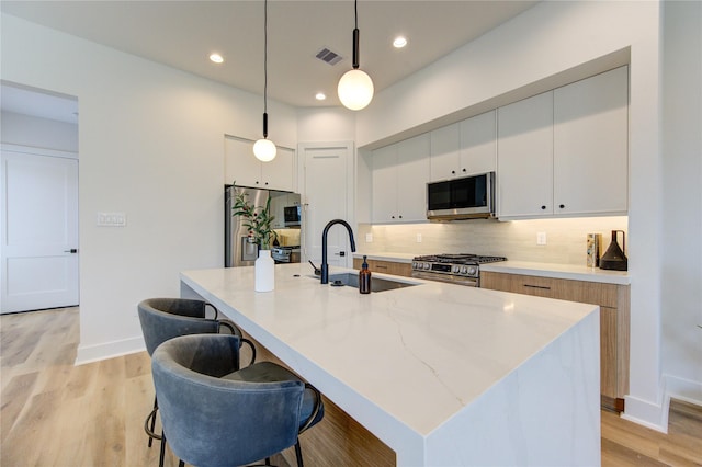 kitchen with hanging light fixtures, appliances with stainless steel finishes, a sink, and a center island with sink