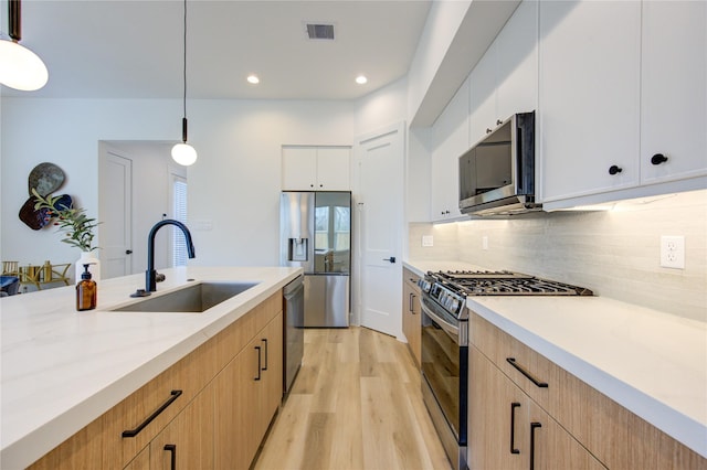 kitchen with hanging light fixtures, white cabinetry, stainless steel appliances, and a sink