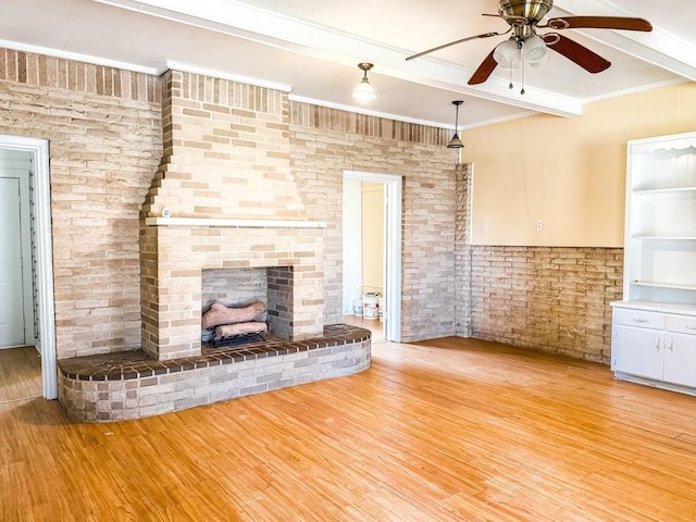 unfurnished living room featuring a fireplace, beamed ceiling, ornamental molding, ceiling fan, and light hardwood / wood-style floors