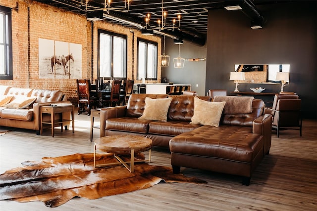 living room featuring a high ceiling, hardwood / wood-style flooring, a chandelier, and brick wall