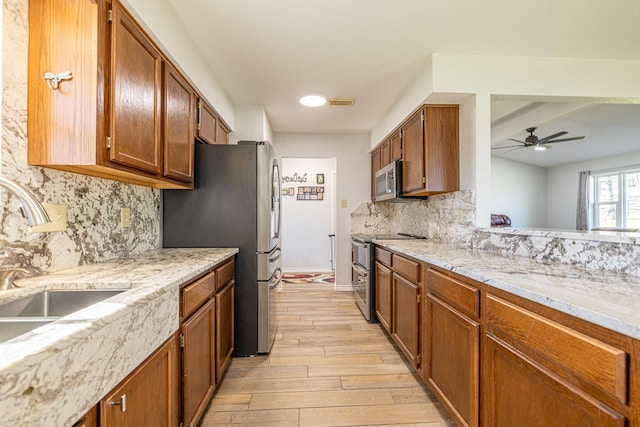 kitchen featuring stainless steel appliances, light wood-type flooring, brown cabinets, and a sink