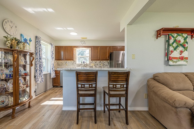 kitchen featuring brown cabinetry, decorative backsplash, light wood-style flooring, a kitchen bar, and stainless steel refrigerator with ice dispenser