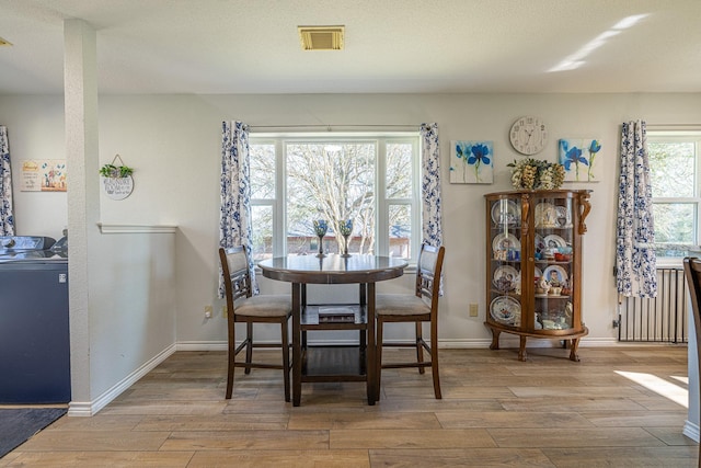 dining space with light wood finished floors, radiator heating unit, visible vents, and baseboards