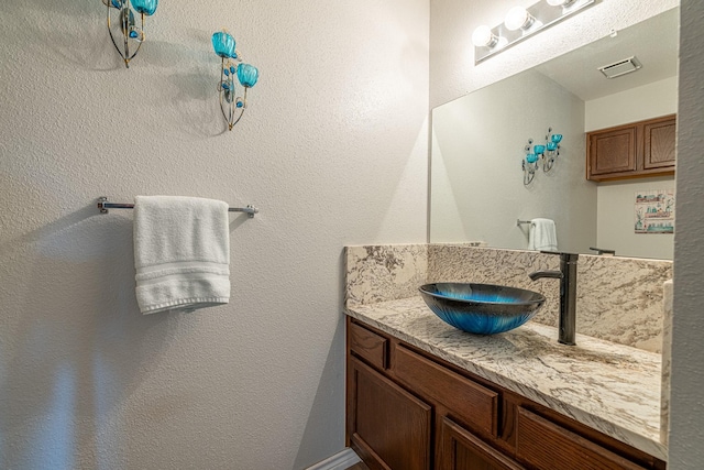 bathroom featuring visible vents, a textured wall, and vanity