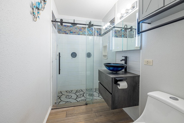 bathroom with a textured wall, toilet, wood finished floors, vanity, and a stall shower