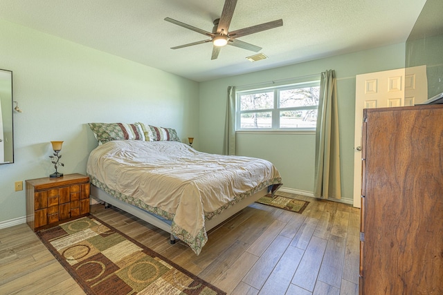 bedroom featuring visible vents, a ceiling fan, a textured ceiling, wood finished floors, and baseboards