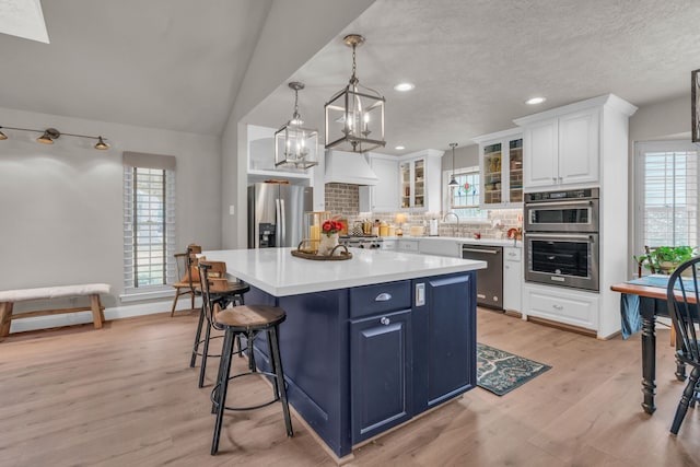 kitchen featuring a kitchen island, appliances with stainless steel finishes, blue cabinets, white cabinets, and decorative backsplash