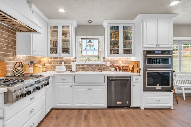 kitchen featuring pendant lighting, sink, white cabinets, stainless steel appliances, and custom range hood