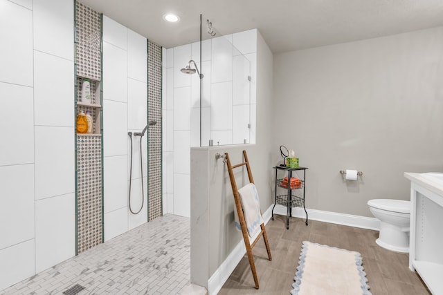 bathroom with a tile shower, vanity, and toilet