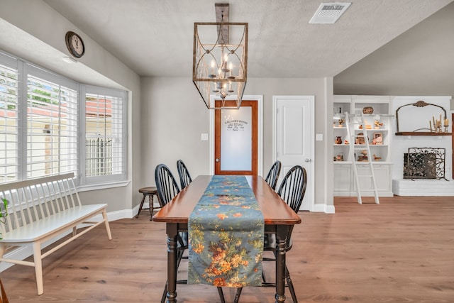 dining space featuring an inviting chandelier, a fireplace, hardwood / wood-style floors, and a textured ceiling