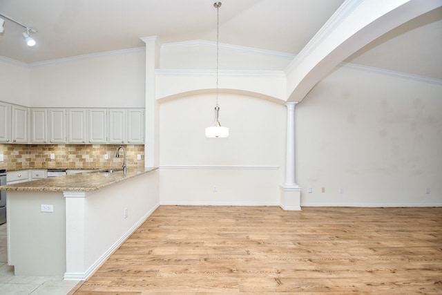 unfurnished dining area featuring arched walkways, crown molding, decorative columns, light wood-style flooring, and a sink