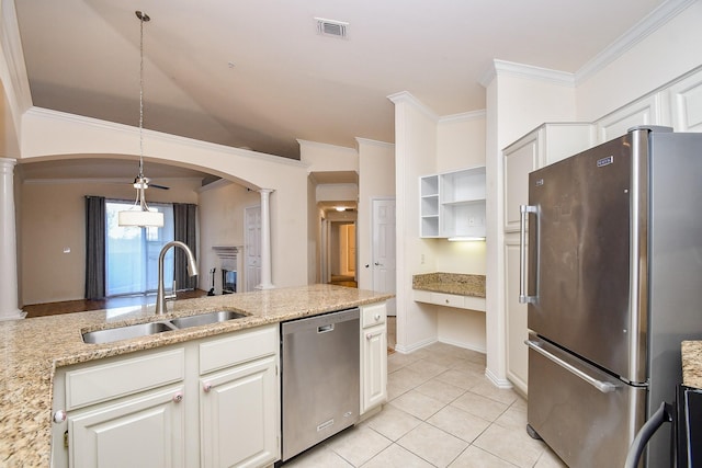 kitchen with arched walkways, a sink, decorative columns, appliances with stainless steel finishes, and ornamental molding