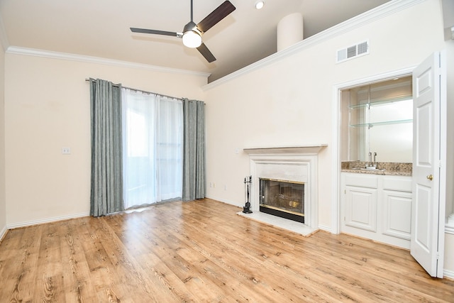 unfurnished living room featuring light wood-type flooring, a glass covered fireplace, visible vents, a ceiling fan, and crown molding