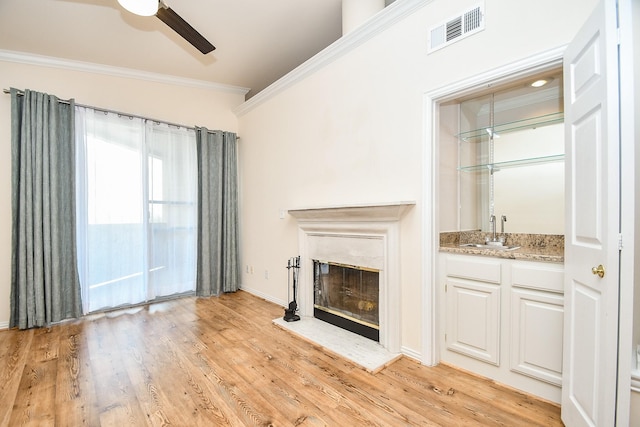 unfurnished living room with wet bar, crown molding, light hardwood / wood-style floors, and ceiling fan