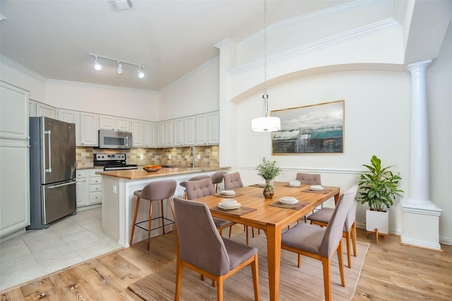 dining area featuring rail lighting, light wood finished floors, and decorative columns