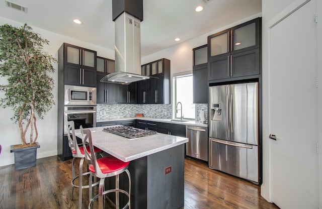 kitchen with a center island, island exhaust hood, stainless steel appliances, backsplash, and glass insert cabinets