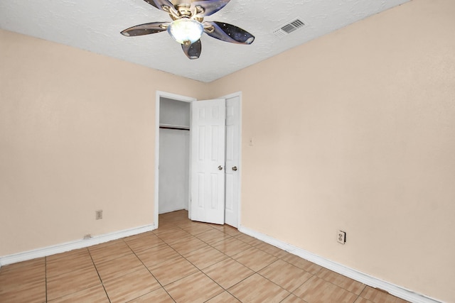 unfurnished bedroom with ceiling fan, light tile patterned floors, a textured ceiling, and a closet