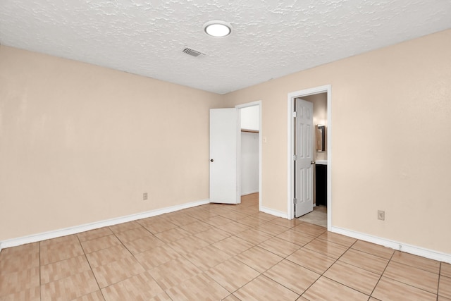 unfurnished bedroom with a spacious closet, light tile patterned floors, a textured ceiling, and a closet