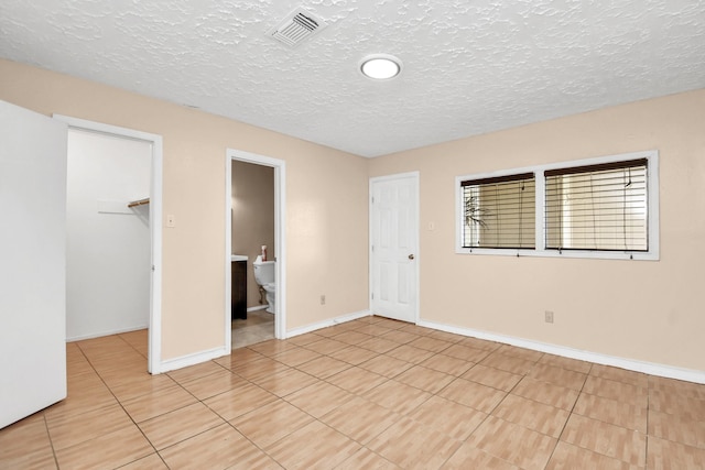 unfurnished bedroom with a walk in closet, light tile patterned floors, a textured ceiling, and a closet