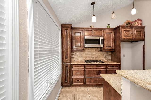 kitchen with lofted ceiling, light stone counters, hanging light fixtures, a textured ceiling, and appliances with stainless steel finishes