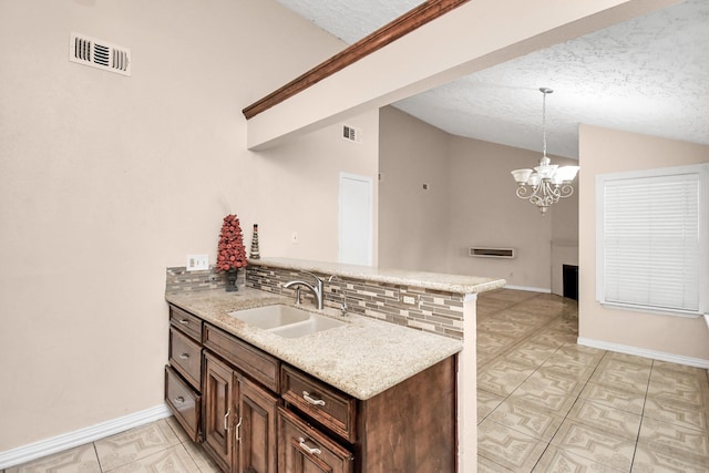 kitchen featuring pendant lighting, sink, lofted ceiling, light stone counters, and kitchen peninsula